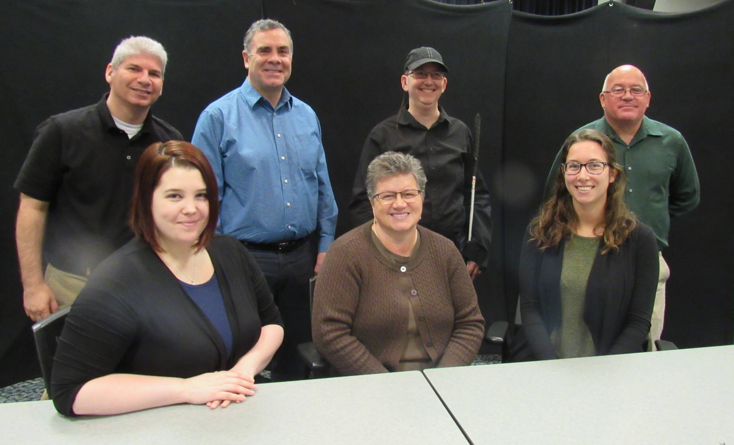 A group of men and women smiling while sitting and standing in front of a black background.