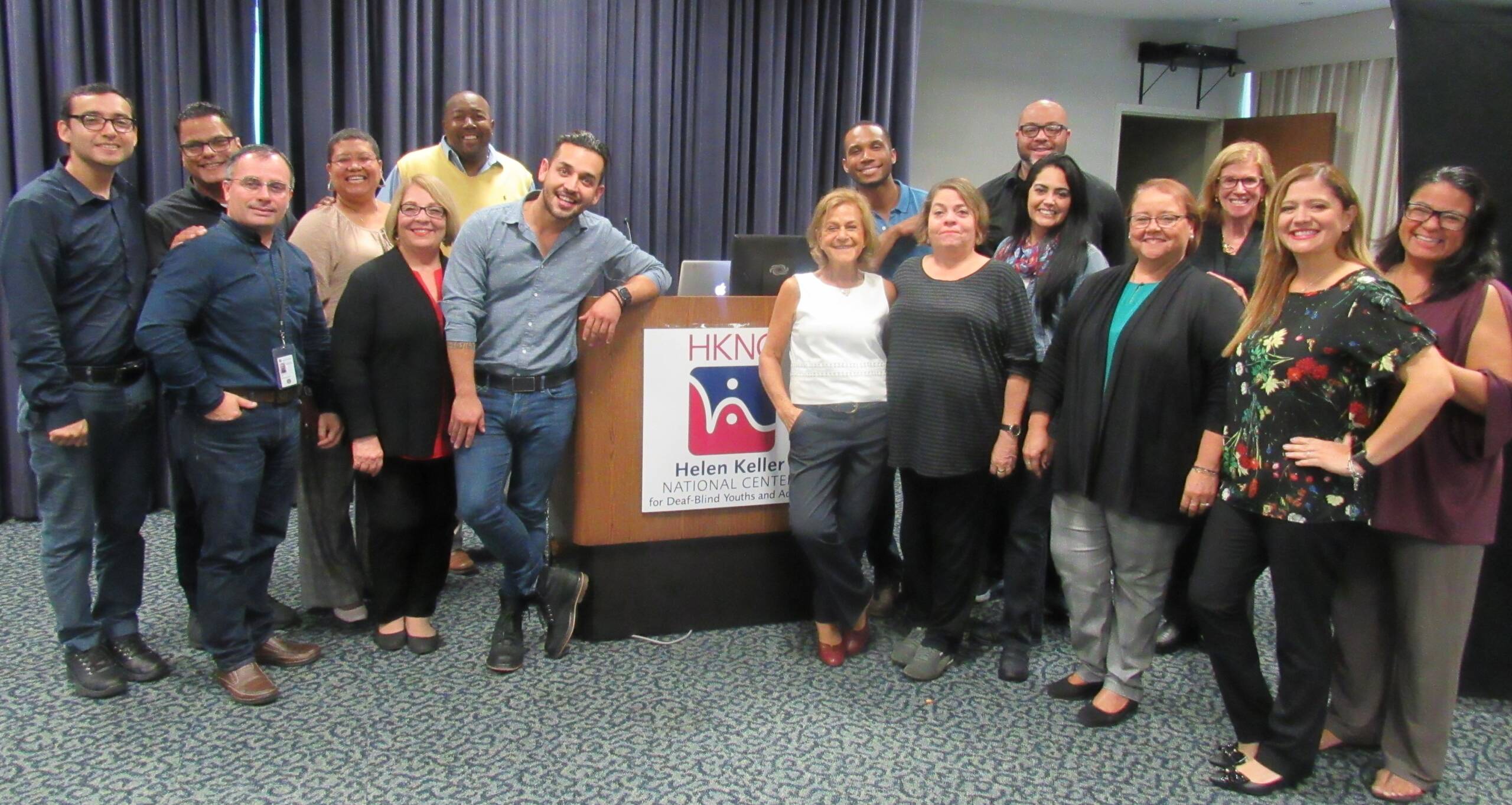 A group of people stand, smiling next to a podium with Helen Keller National Center's logo on it.