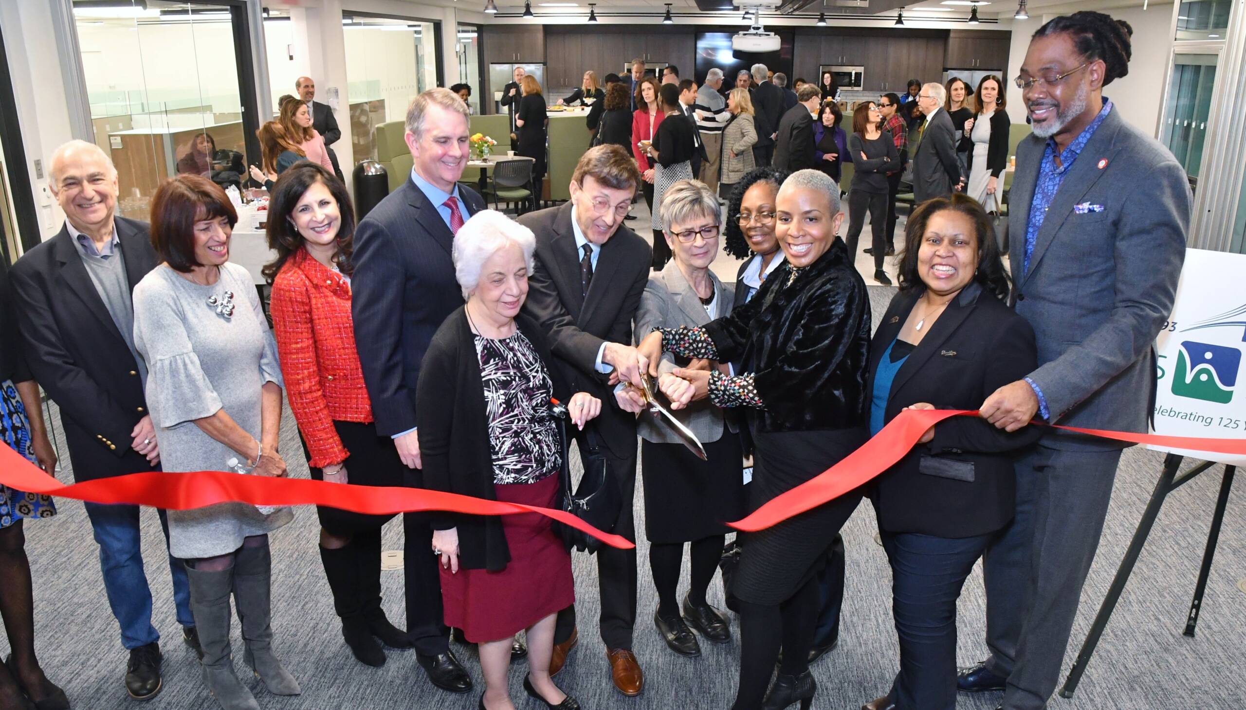 A large group of people cut a red ribbon.