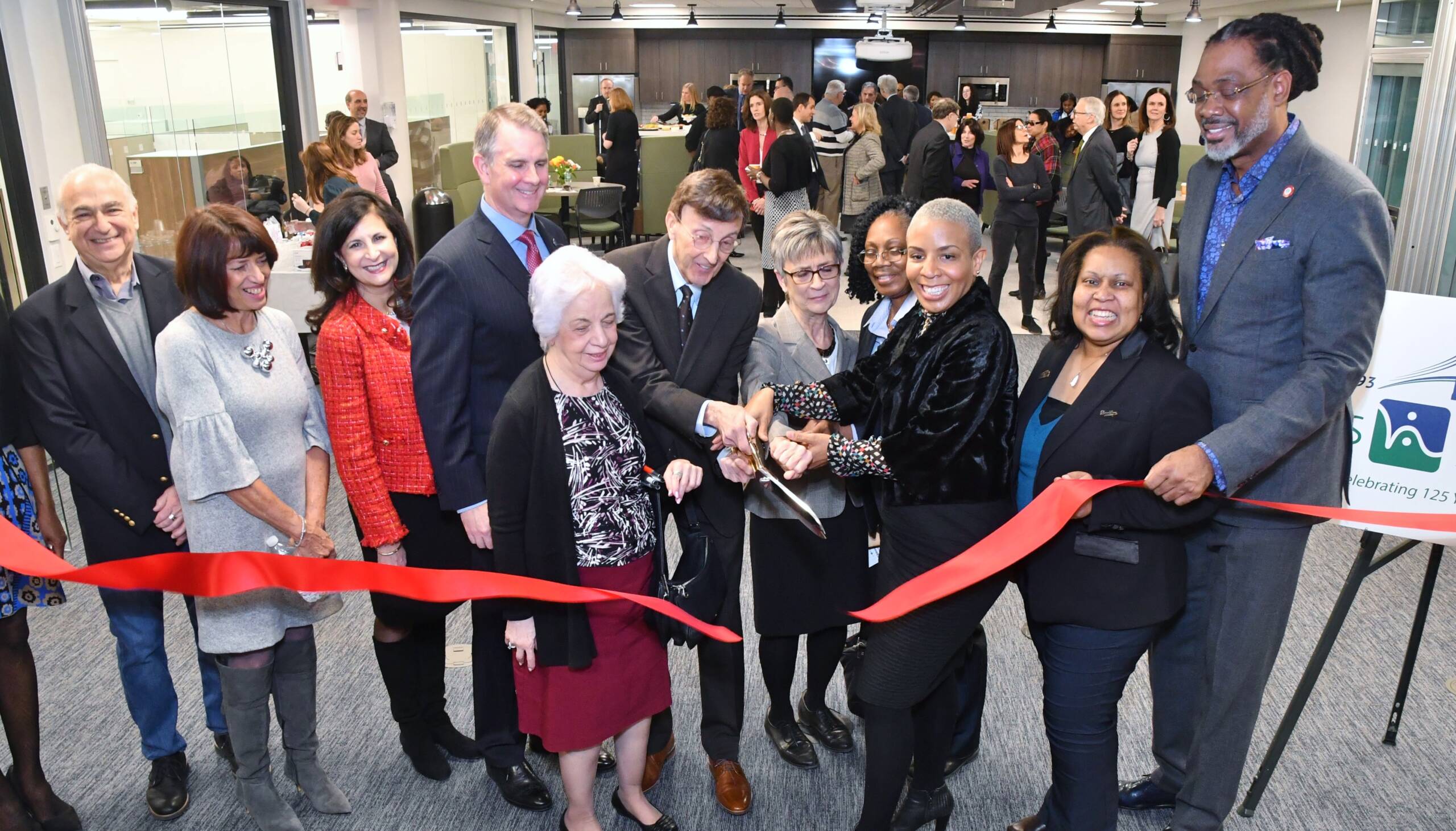 A large group of people cut a red ribbon.