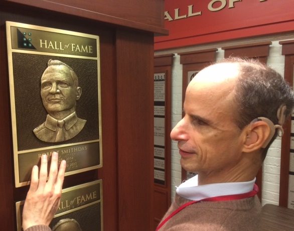 A man with dark brown receding hair touches a bronze plaque with a picture of a man in it.