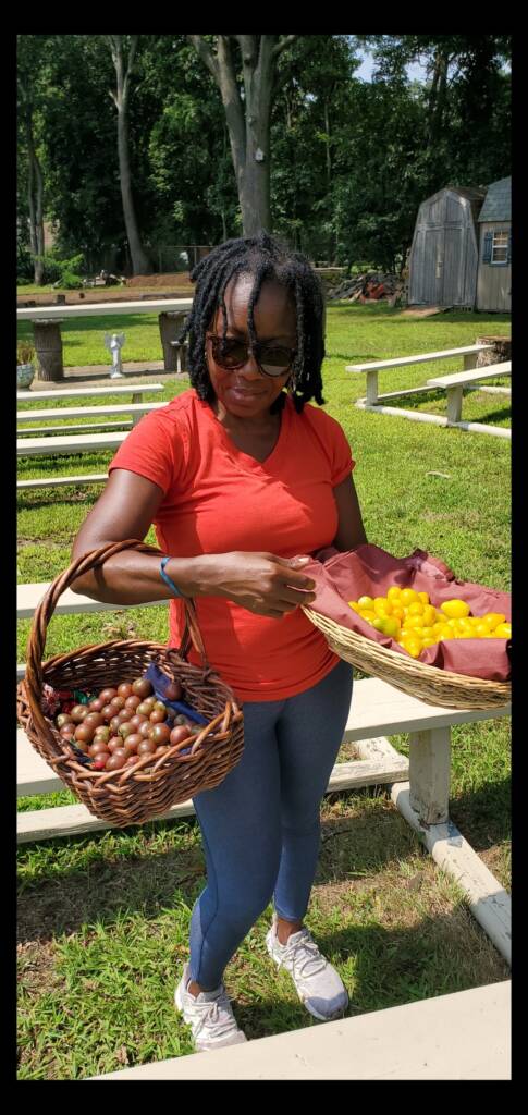 A woman outside wearing sunglasses and holding 2 baskets full of fruit