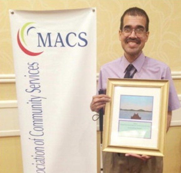 A man named Anthony holding up a framed award next to a sign