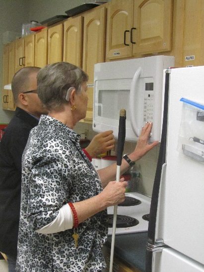 A woman holds a white cane and touches a microwave