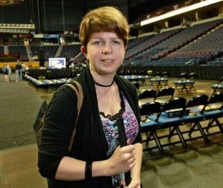 A woman named Quinn standing on the floor of a stadium in front of folding chairs