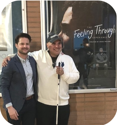 Two men smiling next to the Feeling Through poster