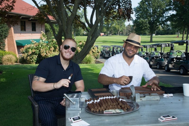 A man with sunglasses and a man with a brown straw hat sit at the Cigar Station.