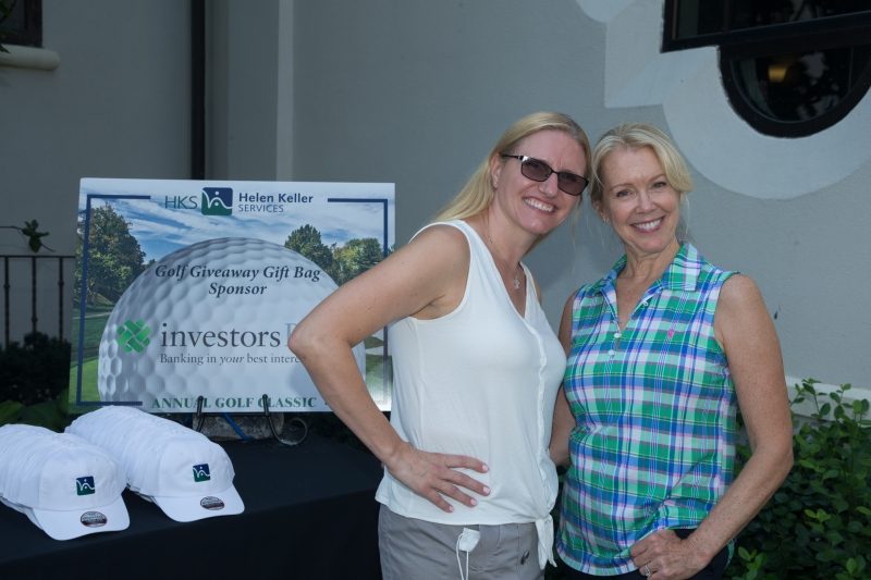 Two woman smiling in front of a banner that has a golf ball with text 