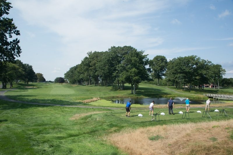 Five individuals swinging their golf club on a golf course.