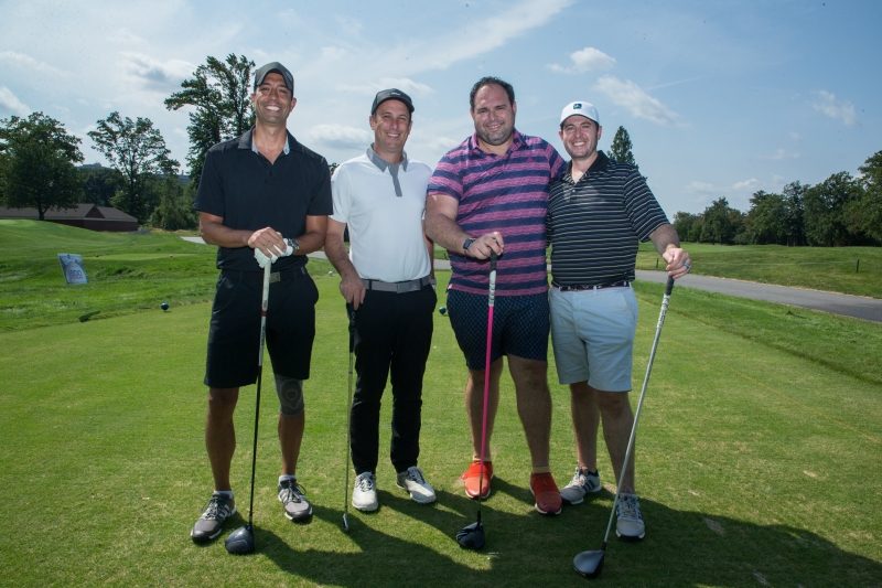 Four men holding their golf clubs and standing on a golf course.
