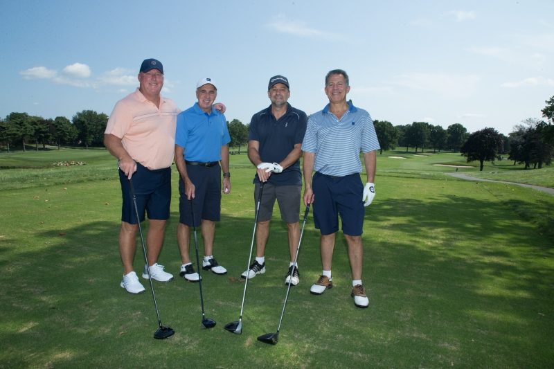 Four men with their golf clubs on a golf course.