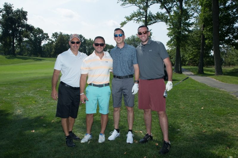 Four men with sunglasses stand together under a tree outdoors.
