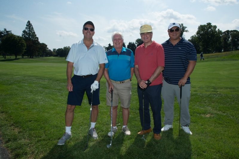 Four men with their golf clubs on a golf course.