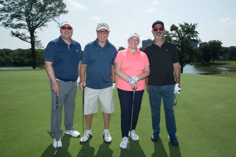 Three men and a woman on a golf course.