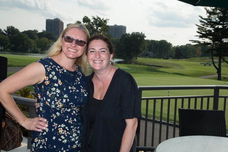 Two woman on a balcony in front of a golf course.