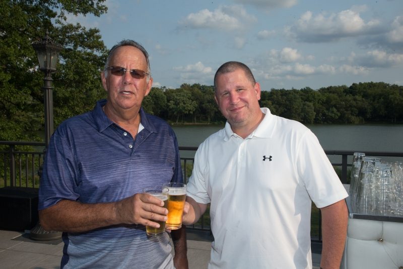Two men with beers. Behind them is a lake.