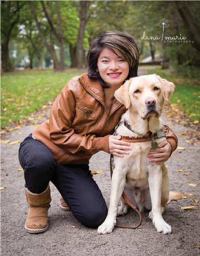 A smiling woman named JaiFei crouching down and hugging her dog named Cruzer outside 