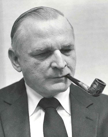 Dr. Robert J. Smithdas wearing a suit and tie with a pipe in his mouth
