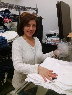 A woman named Connie smiling and touching a pile of white shirts