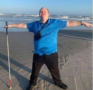 Scott Davert standing in the sand on the beach and holding a white cane