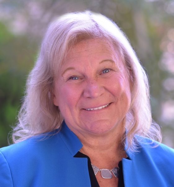 Head shot of a woman with light skin and shoulder length blonde hair wearing a bright blue jacket