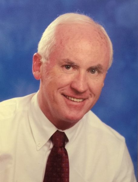 Head shot of a man with light skin and receding gray hair wearing a white shirt and red tie