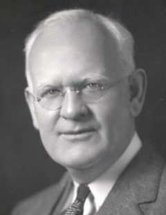 Peter J Salmon looking into the camera and wearing a suit, tie, and glasses