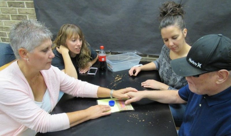 Group of people sitting at a table while a woman and man touch an object in the center of the table together