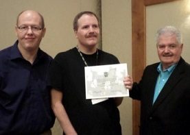 Scott, center, displays his award next to 2 men