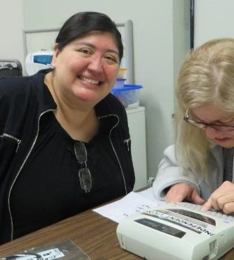 Two women, one smiling into the camera and the other using a label machine