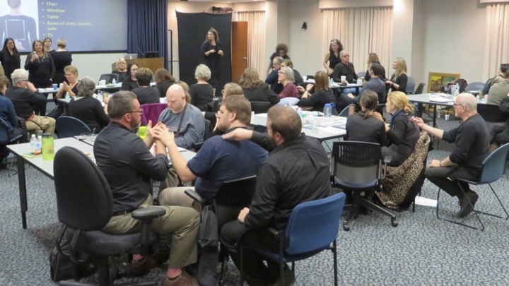 Group of men and women sitting at tables and signing in a large room