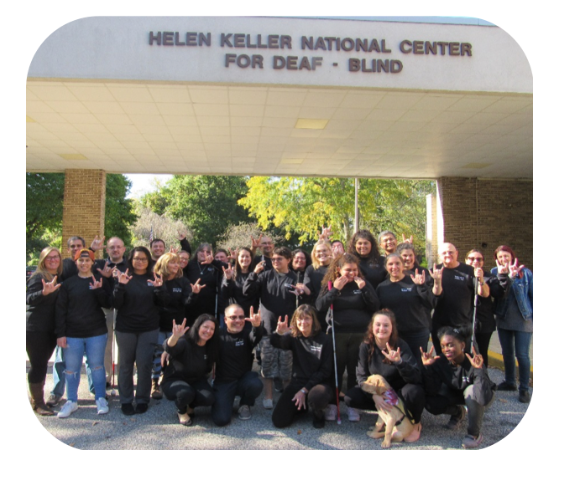 Group of people signing I Love You in front of the Helen Keller National Center