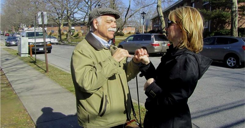 A man signing to a woman outdoors.
