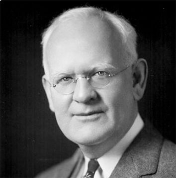 Dr. Peter J. Salmon looking into the camera while wearing a suit, tie, and circular rimless eyeglasses