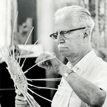 An older man wearing glasses and weaving a basket