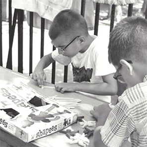 2 boys sitting at a table outside creating figurines next to “Shapees” box
