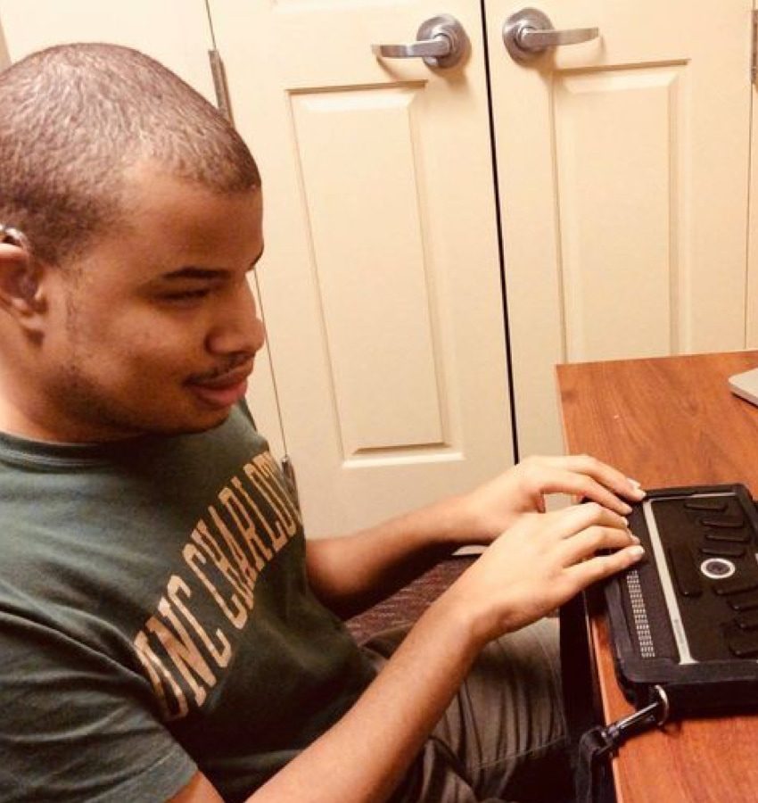 Man with hearing aid touching a braille display at a desk