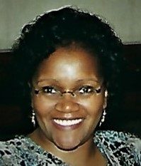 A black woman with glasses smiling into the camera