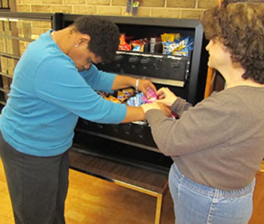 Two women adding snacks to a vending machine 