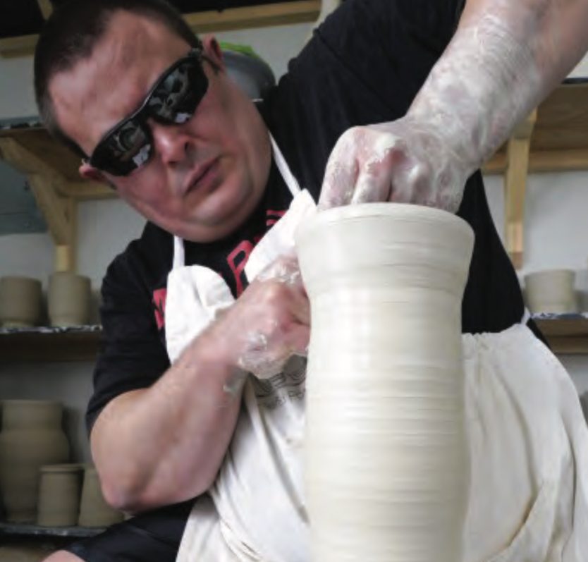 Man wearing sunglasses and apron shaping pottery