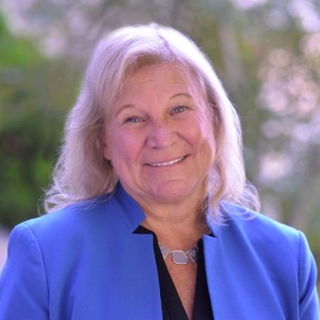 Sue Ruzenski wearing a light blue suit jacket and smiling into the camera outside