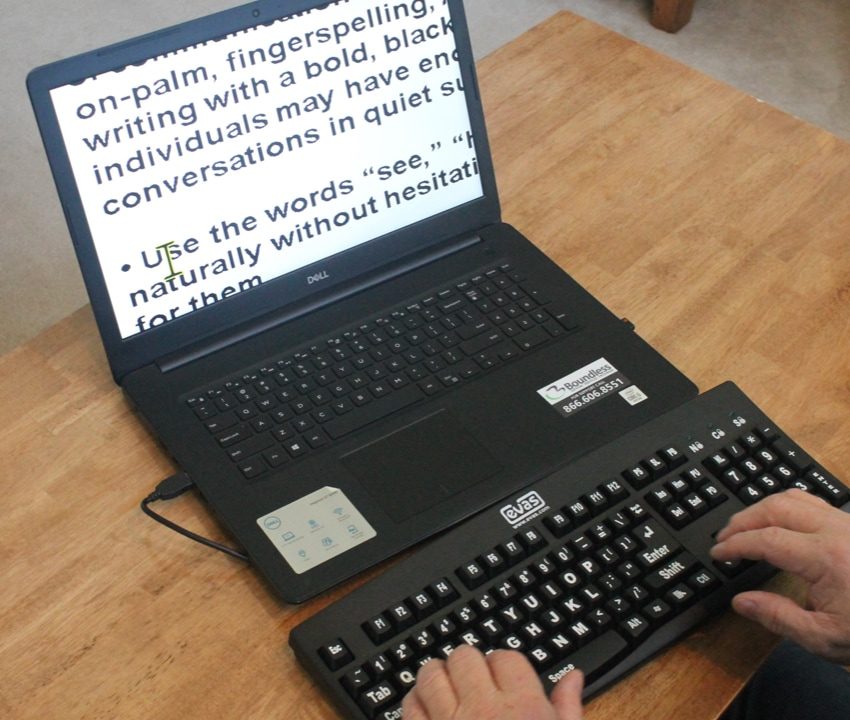 A person typing on a laptop using an external keyboard. Large words project on the laptop screen