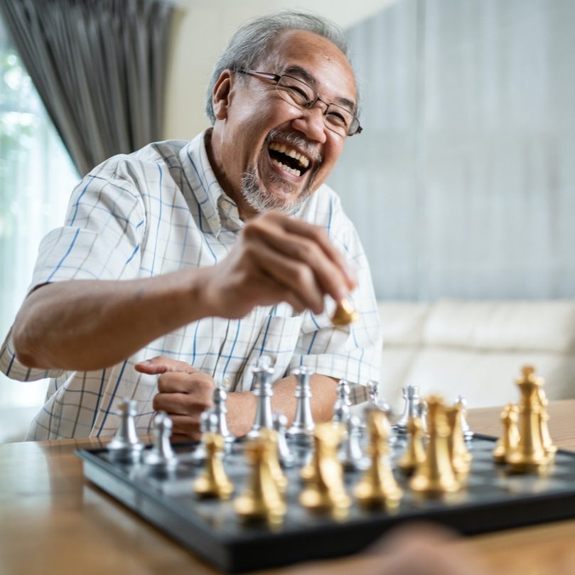 Middle-aged man smiling jovially and playing chess. He is taking a chess piece from his opponent 