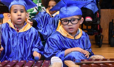 Three pre-school aged kids wearing blue graduation caps and gowns