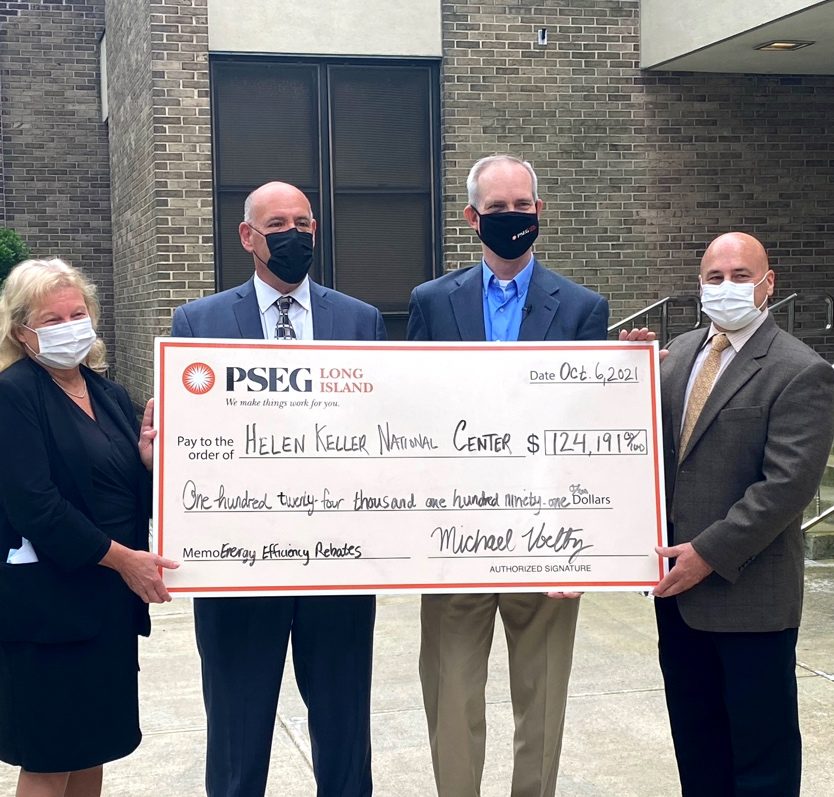 3 men and a woman in business attire stand and hold an oversized check from PSEG made to Helen Keller National Center for $124,191