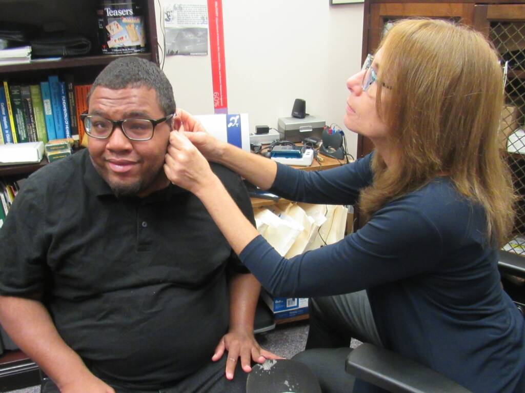 Female staff member adjusting man’s hearing aid