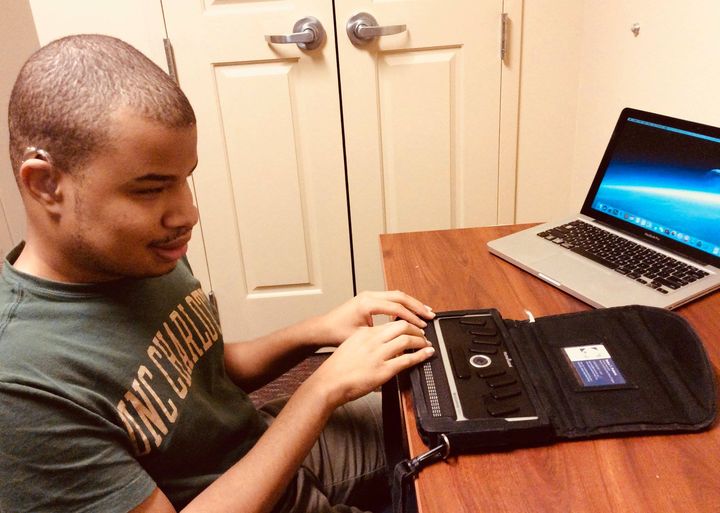 Man with hearing aid using braille display on laptop