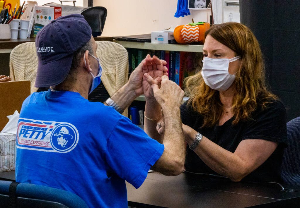 A man and a woman sit facing each other and use tactile hand over hand sign 