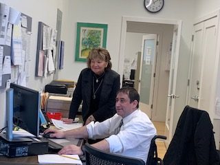 A man named Charles Fulham typing on a computer keyboard next to a woman wearing black standing next to him