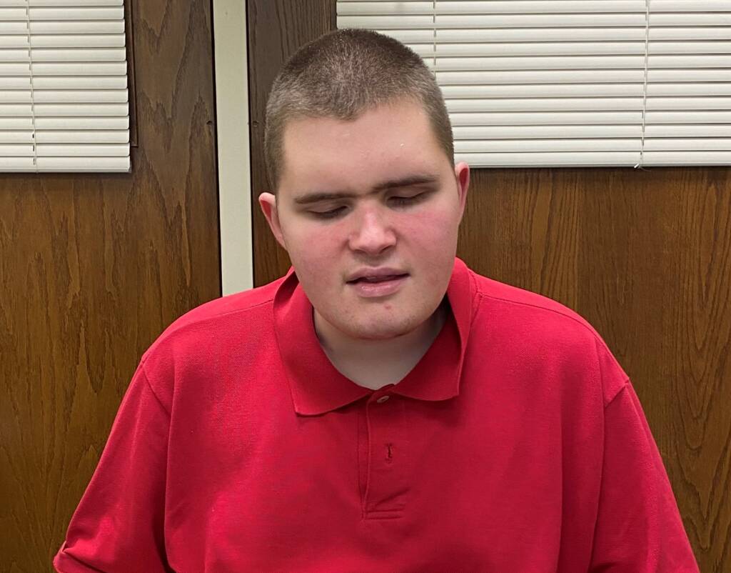 A boy named Rocky wearing a red collared shirt looking down